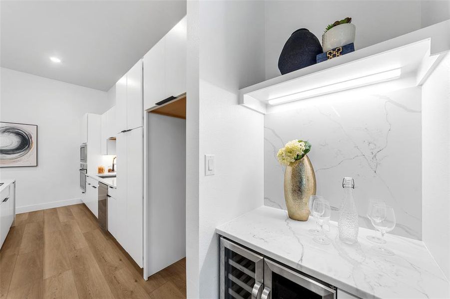 Kitchen featuring white cabinets, light wood-style floors, wine cooler, light stone counters, and modern cabinets Kitchen featuring white cabinets, light wood-style floors, wine cooler, light stone counters, and modern cabinets