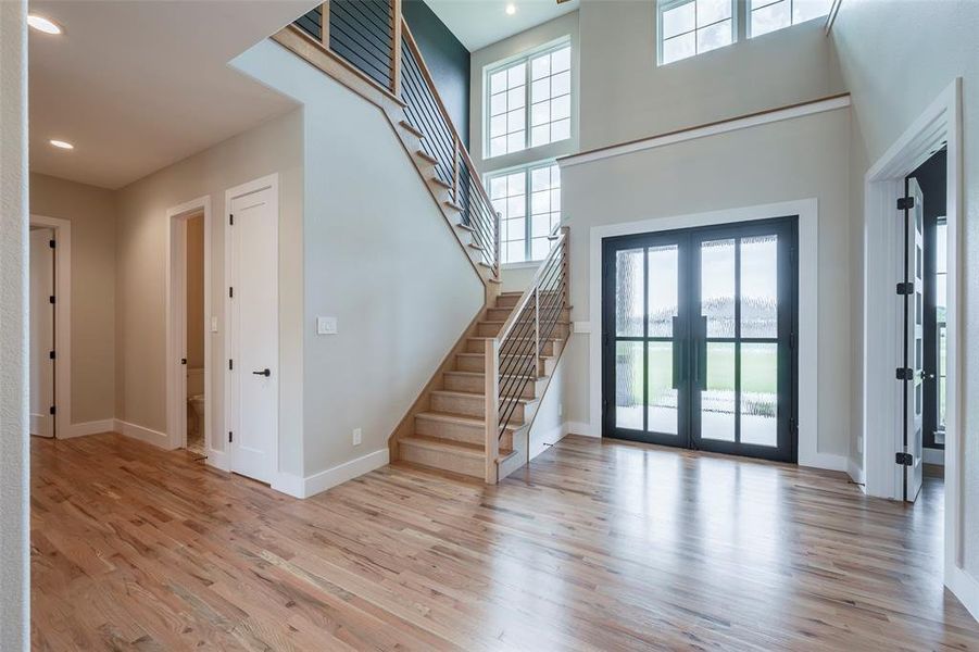 Foyer entrance featuring french doors, a towering ceiling, stairway, light wood-type flooring, and recessed lighting