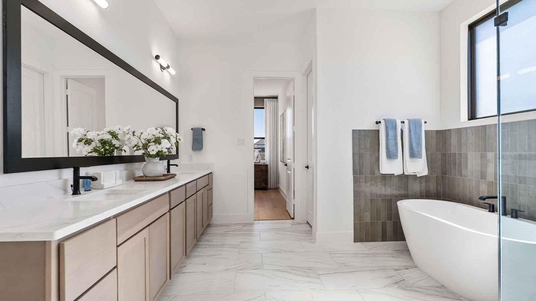 Luxurious primary bathroom with dual vanities, a soaking tub, and separate glass-enclosed walk in shower