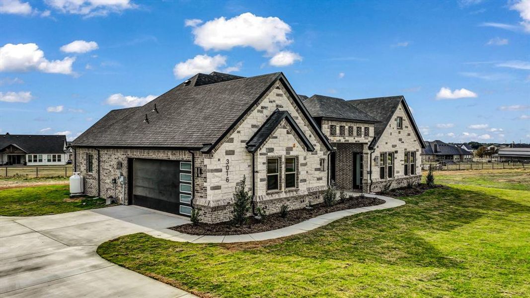 View of front facade with driveway, a garage, brick siding, and stone siding