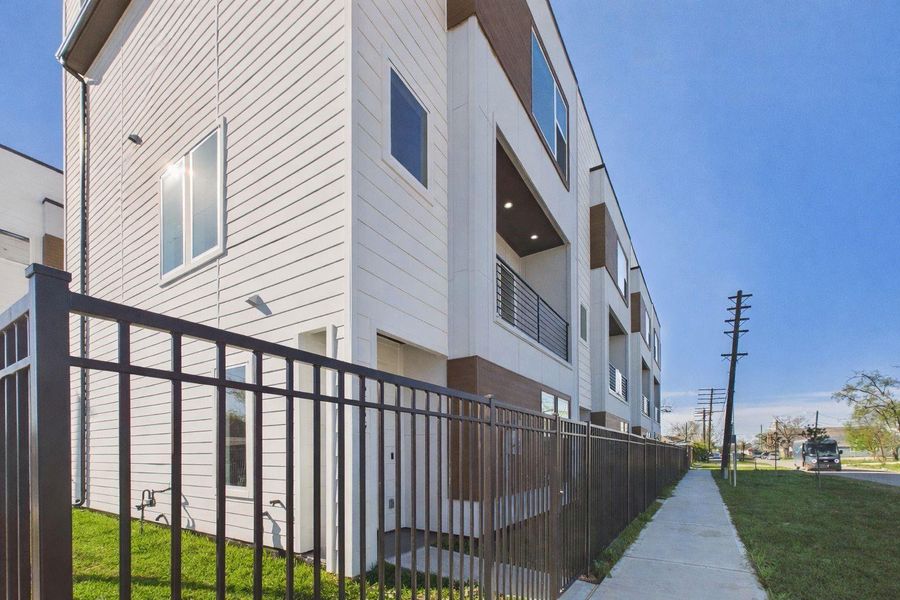 Modern townhouse with a sleek design featuring large windows and a private balcony. It's surrounded by a secure fence and has a sidewalk leading to the entrance, set in a spacious outdoor area. Modern townhouse with a sleek design featuring large windows and a private balcony. It's surrounded by a secure fence and has a sidewalk leading to the entrance, set in a spacious outdoor area.