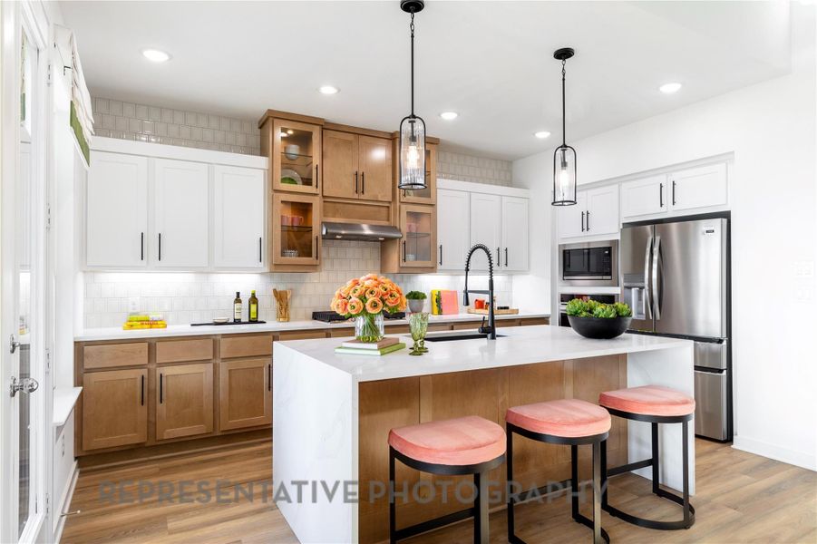 Kitchen featuring stainless steel fridge, built in microwave, light countertops, light wood-style floors, and brown cabinets