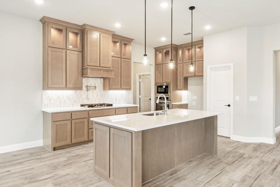 Kitchen with tan wood cabinets, center island with sink, pendant lights, and light wood-look tile floors