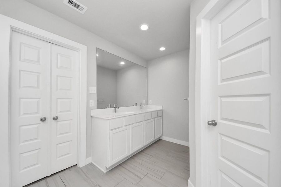 Features a spacious double-sink vanity with ample counter space and a large mirror, providing plenty of room for daily routines along with convenient storage just steps from the walk-in closet.