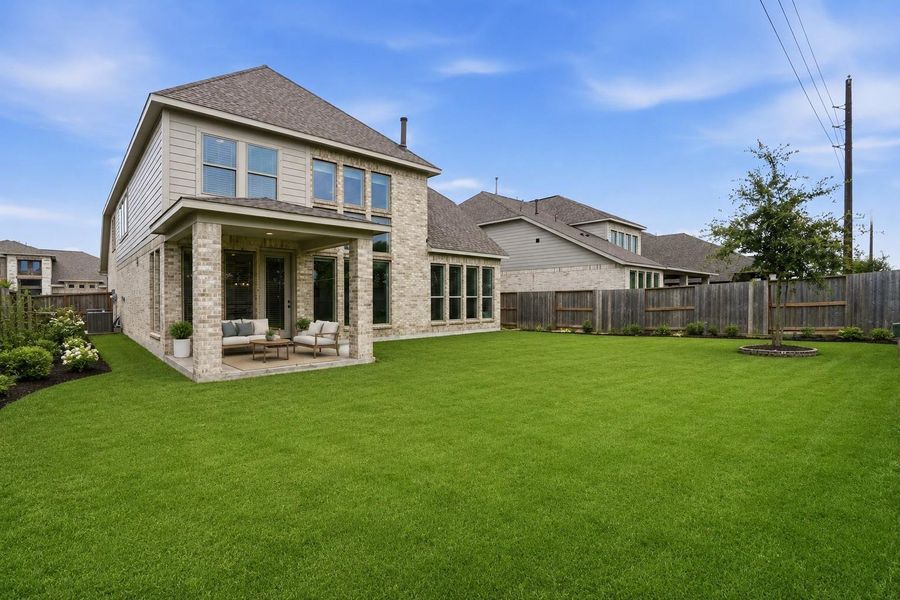 This virtually staged photo showcases a spacious backyard with a well-maintained lawn, a modern two-story brick house, and a cozy covered patio perfect for outdoor relaxation. The area is fenced, providing privacy and security. This virtually staged photo showcases a spacious backyard with a well-maintained lawn, a modern two-story brick house, and a cozy covered patio perfect for outdoor relaxation. The area is fenced, providing privacy and security.