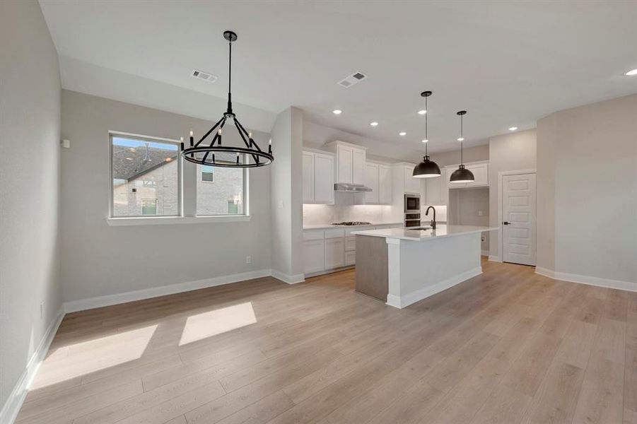 Kitchen with white cabinetry, an island with sink, hanging lights, light wood-style floors, and light stone counters