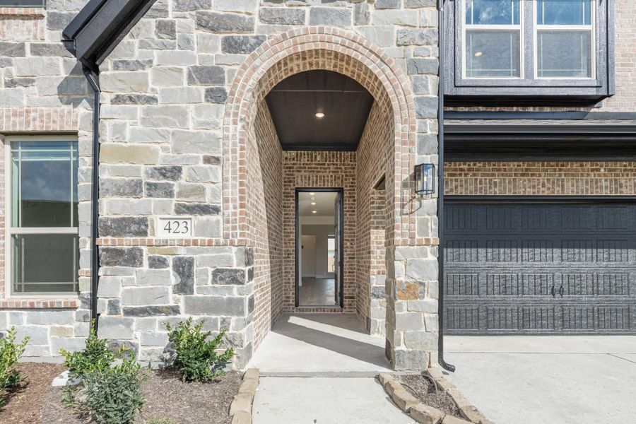 Home entrance with brick arched entryway, stone exterior, and dark front door with covered porch
