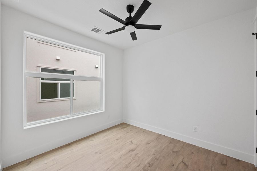 Room featuring a wide window, wood-finish flooring, and a black ceiling fan with an integrated light
