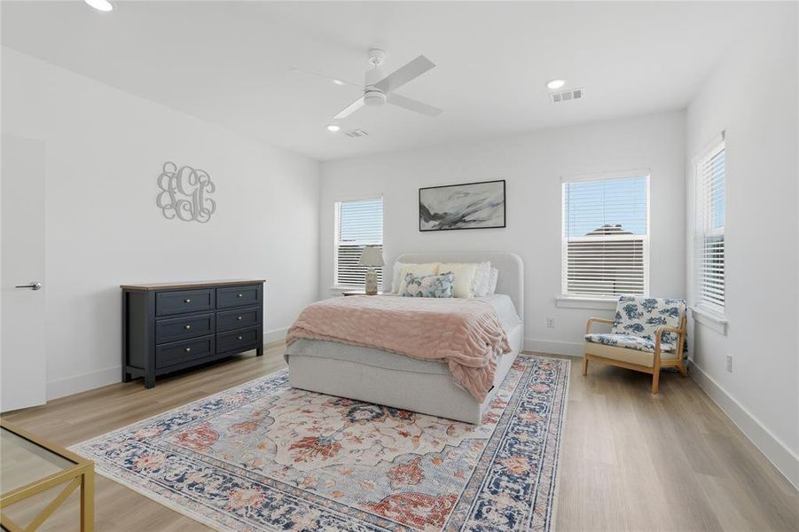 Spacious bedroom featuring light wood-finish flooring, multiple windows providing natural light, recessed lighting, and a ceiling fan