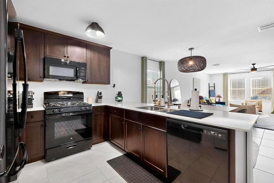 Kitchen with dark brown cabinetry, open floor plan, black appliances, and plenty of natural light Kitchen with dark brown cabinetry, open floor plan, black appliances, and plenty of natural light