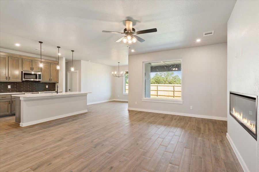 Unfurnished living room with a glass covered fireplace, light wood-style flooring, ceiling fan, recessed lighting, and a chandelier