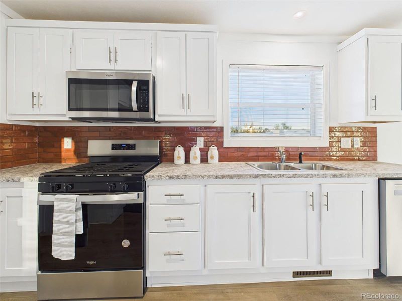 A closer look at the kitchen reveals a Whirlpool gas range, built-in microwave, and large sink beneath a picture window offering natural light.