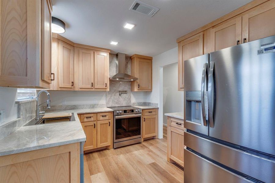 Kitchen featuring wall chimney exhaust hood, sink, light hardwood / wood-style flooring, light brown cabinets, and stainless steel appliances