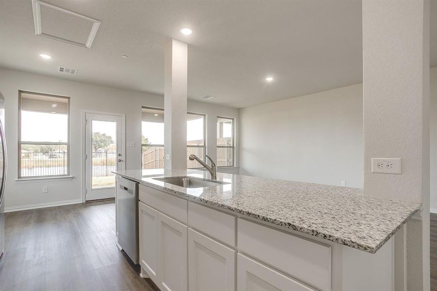 Kitchen featuring dark wood-type flooring, white cabinetry, light stone countertops, stainless steel dishwasher, and recessed lighting