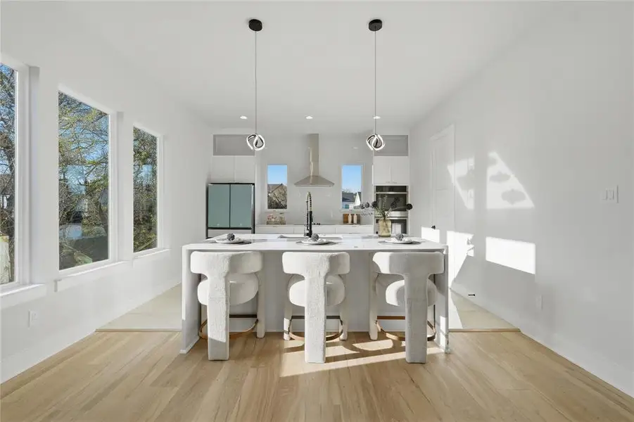 Kitchen featuring white cabinetry, a kitchen bar, a center island with sink, light wood-style floors, and decorative light fixtures Kitchen featuring white cabinetry, a kitchen bar, a center island with sink, light wood-style floors, and decorative light fixtures