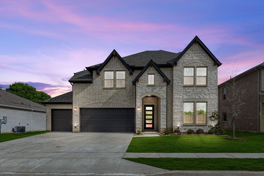 Two-story stone home with two-car garage, arched entry, and manicured front lawn at dusk