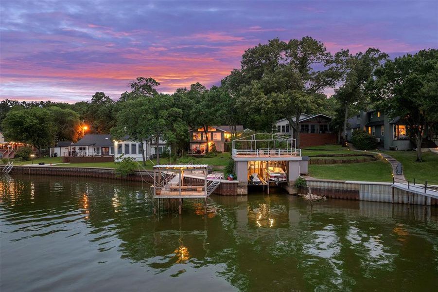 Waterfront property featuring multiple boat docks, a two-story boat house with upper deck, permanent seawall, and mature trees