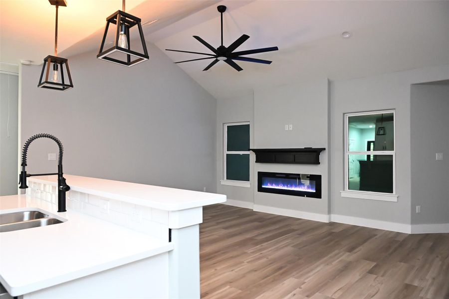 Kitchen featuring a kitchen island with sink, vaulted ceiling, a glass covered fireplace, dark wood-type flooring, and open floor plan