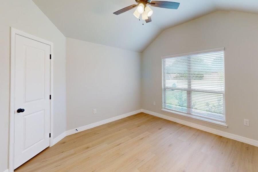 Empty room featuring light wood-style floors, ceiling fan, and lofted ceiling