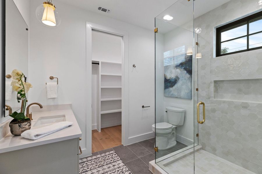Bathroom featuring a stall shower, double vanity, tile patterned floors, toilet, and a spacious closet