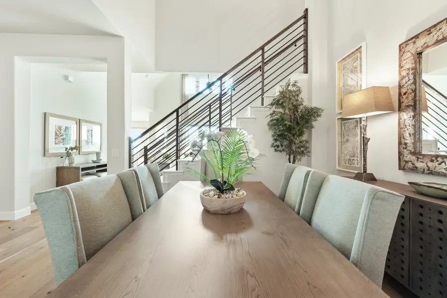 Dining room with long wood table, light blue upholstered chairs, and staircase with metal railing in background