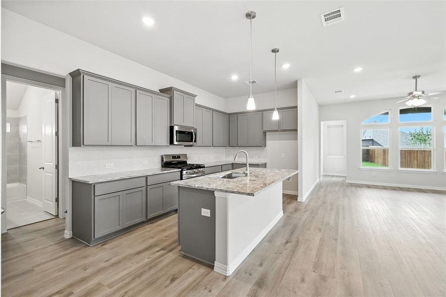 Kitchen with gray cabinets, light stone counters, stainless steel appliances, and light wood-style flooring