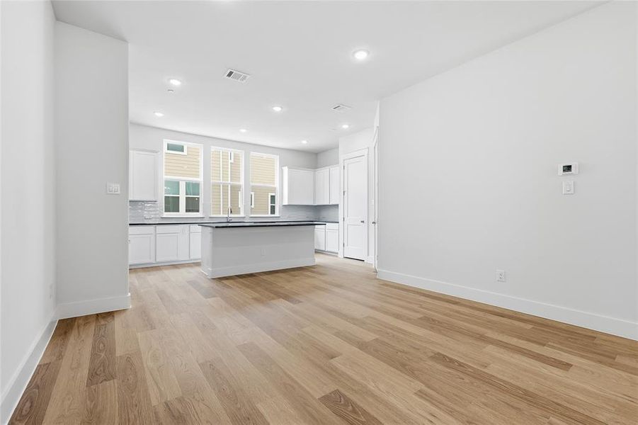Living area featuring light wood flooring, recessed lighting, and a modern kitchen with white cabinetry and an island
