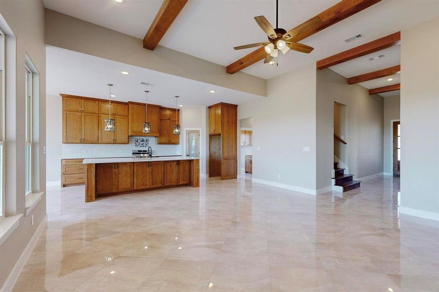 Kitchen featuring tasteful backsplash, ceiling fan, pendant lighting, beamed ceiling, and a center island with sink