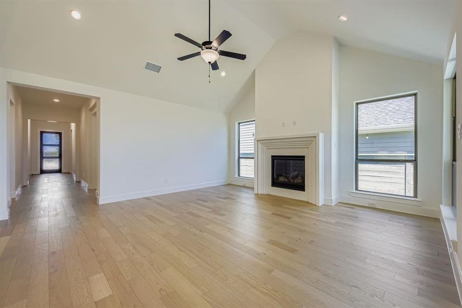 Unfurnished living room with high vaulted ceiling, light wood finished floors, a glass covered fireplace, ceiling fan, and recessed lighting Unfurnished living room with high vaulted ceiling, light wood finished floors, a glass covered fireplace, ceiling fan, and recessed lighting