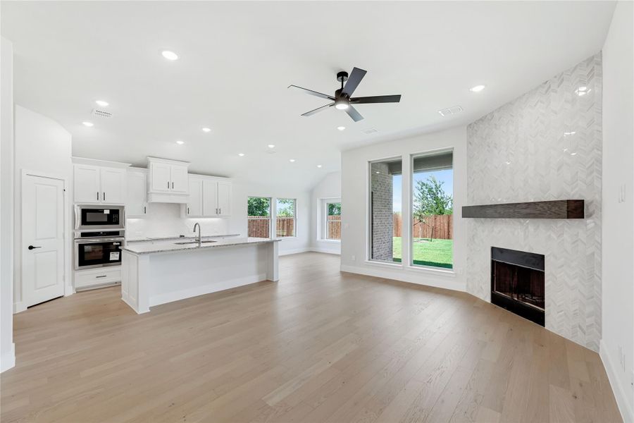 Open-concept living area with kitchen island, tile fireplace, hardwood floors, and ceiling fan