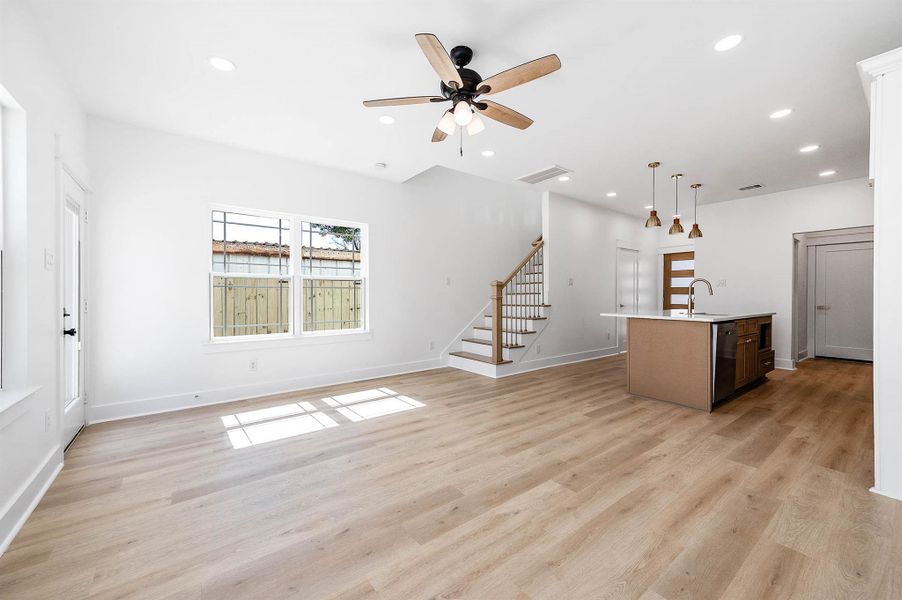 Open living space featuring wood-style flooring, recessed lighting, and a seamless view into the kitchen.