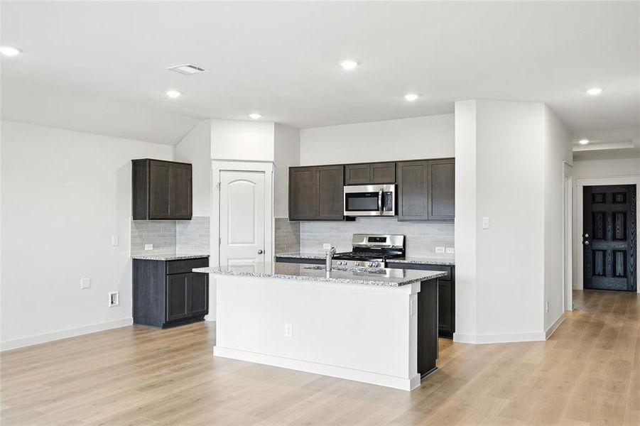 Kitchen featuring decorative backsplash, light stone counters, appliances with stainless steel finishes, dark brown cabinetry, and recessed lighting Kitchen featuring decorative backsplash, light stone counters, appliances with stainless steel finishes, dark brown cabinetry, and recessed lighting