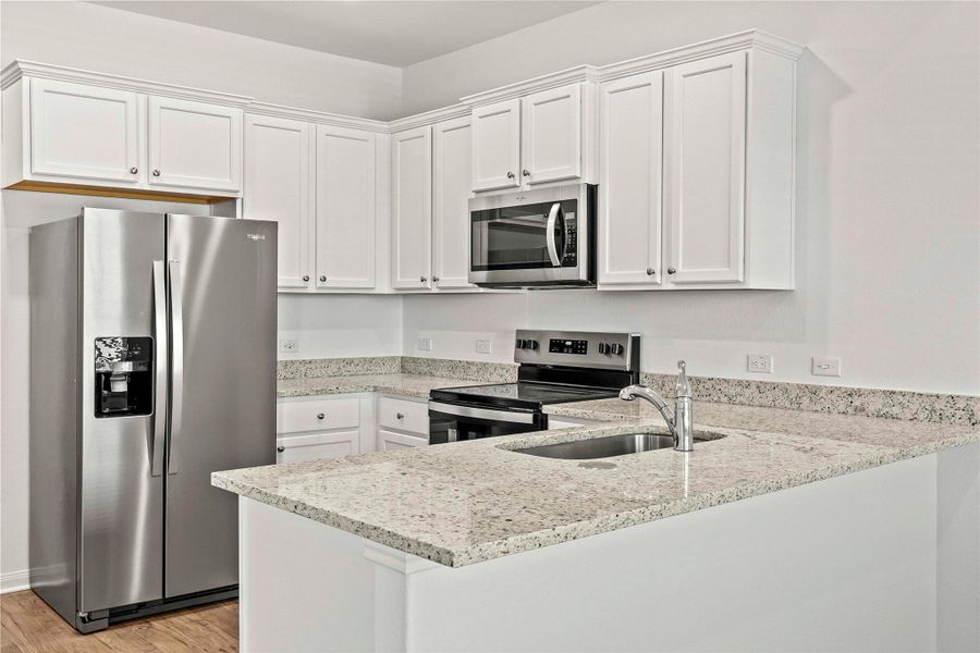 Kitchen with stainless steel appliances, white cabinets, light stone counters, a peninsula, and light wood finished floors Kitchen with stainless steel appliances, white cabinets, light stone counters, a peninsula, and light wood finished floors