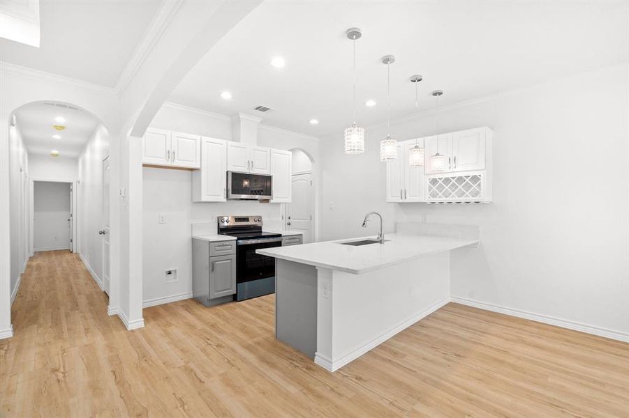Kitchen featuring stainless steel appliances, a peninsula, light wood-type flooring, light countertops, and ornamental molding Kitchen featuring stainless steel appliances, a peninsula, light wood-type flooring, light countertops, and ornamental molding