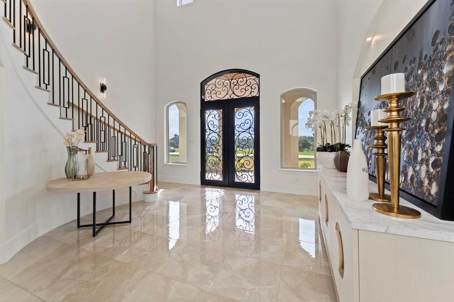 Another view of this elegant entryway featuring a grand staircase with modern metal balusters, high ceilings, and polished tile flooring. The front door has ornate wrought-iron detailing, and the space is well-lit with natural light from large windows. Stylish décor by Star Furniture the area accents, adding a touch of sophistication.