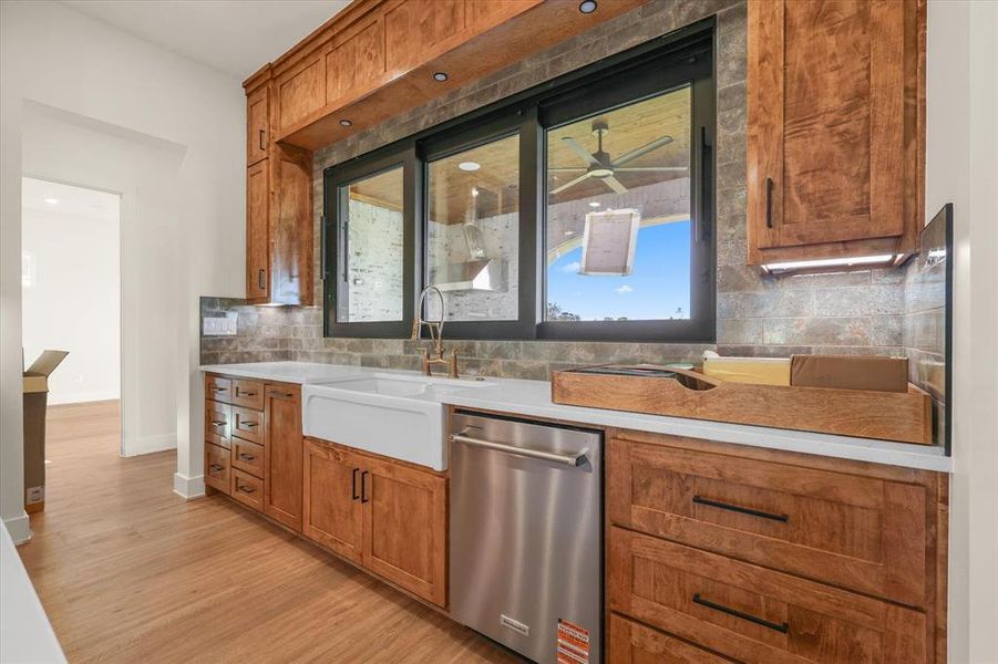 Kitchen featuring brown cabinetry, tasteful backsplash, stainless steel dishwasher, light wood-style flooring, and a ceiling fan