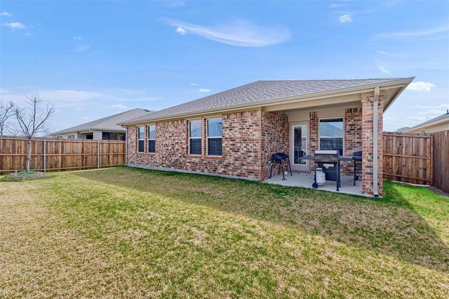 Rear view of house featuring a fenced backyard, a lawn, a patio area, and brick siding