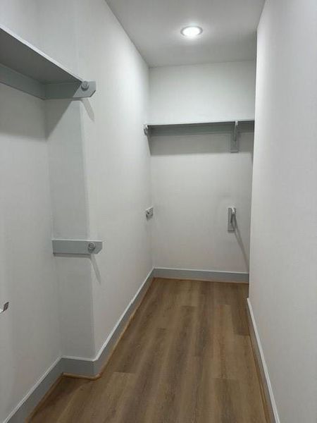 This is a neat, empty walk-in closet with built-in shelves and hanging rods, featuring wood flooring and good overhead lighting.