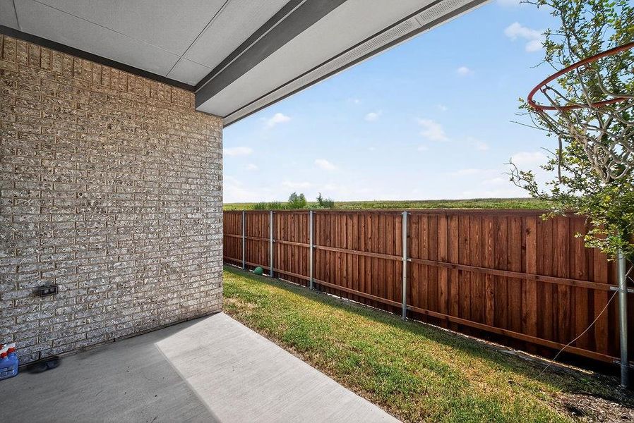 Covered patio with a concrete slab, brick exterior, wood privacy fence, and a grass lawn