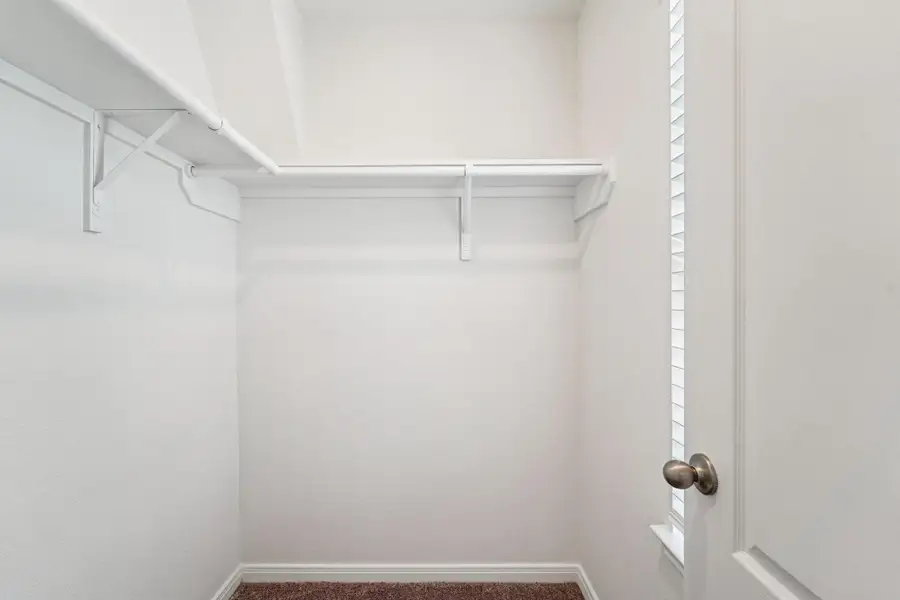 A clean and simple walk-in closet in the secondary bedroom, complete with essential rods and built-in shelving to maximize storage.