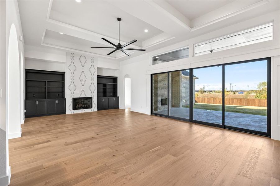 Unfurnished living room with a raised ceiling, light wood-style flooring, ceiling fan, arched walkways, and a fireplace Unfurnished living room with a raised ceiling, light wood-style flooring, ceiling fan, arched walkways, and a fireplace