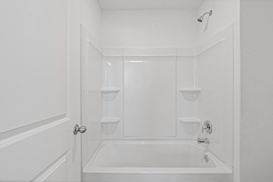 A clean bathtub and shower combination features integrated shelving.