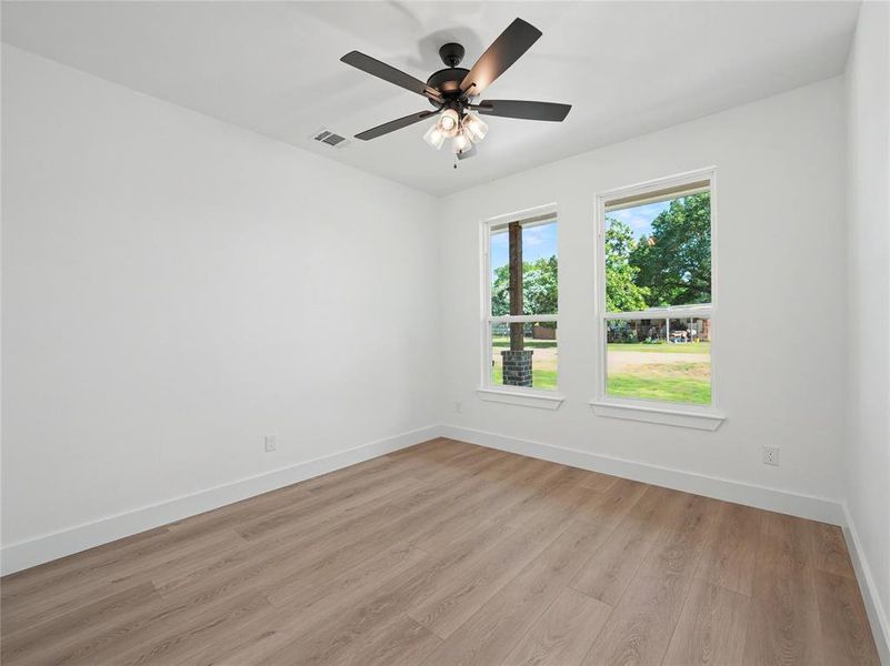 Light-filled interior space featuring two windows, wood-finish flooring, and a ceiling fan with integrated lighting Light-filled interior space featuring two windows, wood-finish flooring, and a ceiling fan with integrated lighting