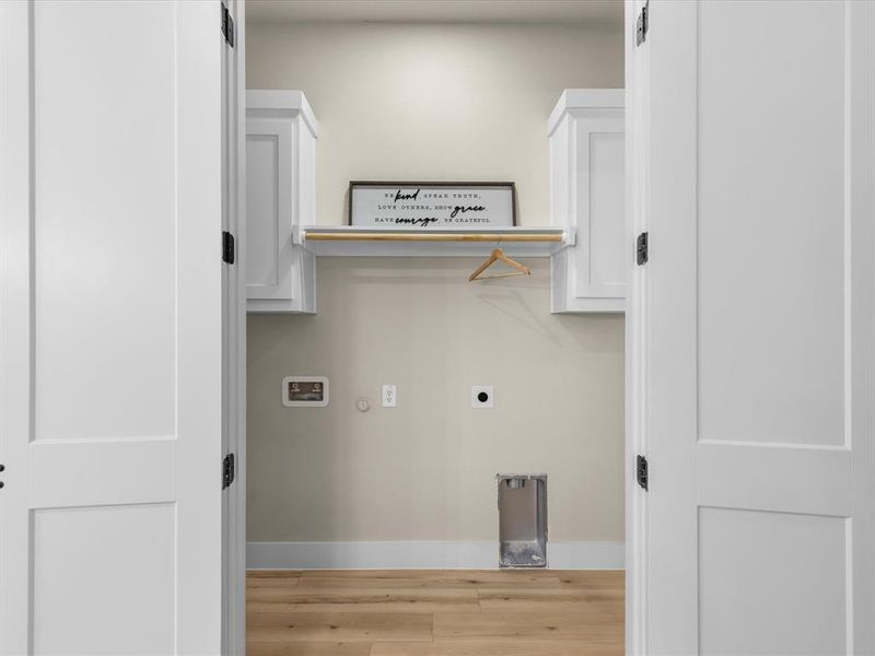 Laundry area featuring two-panel white doors, light wood-finish flooring, and white upper cabinetry