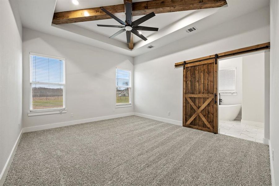 Spare room featuring a barn door, visible vents, baseboards, a ceiling fan, and a tray ceiling