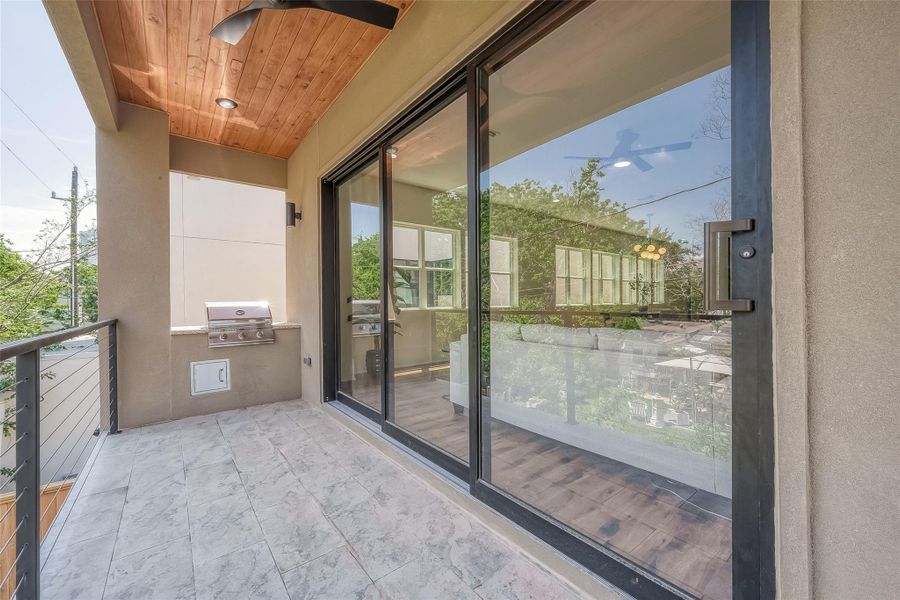 This is a cozy, well-lit outdoor patio with a built-in grill, featuring a wooden ceiling that adds warmth to the space. Large glass doors provide a seamless transition to the indoors, and the balcony offers a view of the surrounding greenery. This is a cozy, well-lit outdoor patio with a built-in grill, featuring a wooden ceiling that adds warmth to the space. Large glass doors provide a seamless transition to the indoors, and the balcony offers a view of the surrounding greenery.