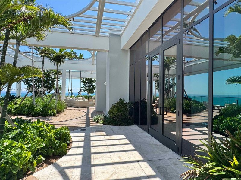 Expansive outdoor terrace featuring mature palm trees, lush landscaping, and a slatted pergola