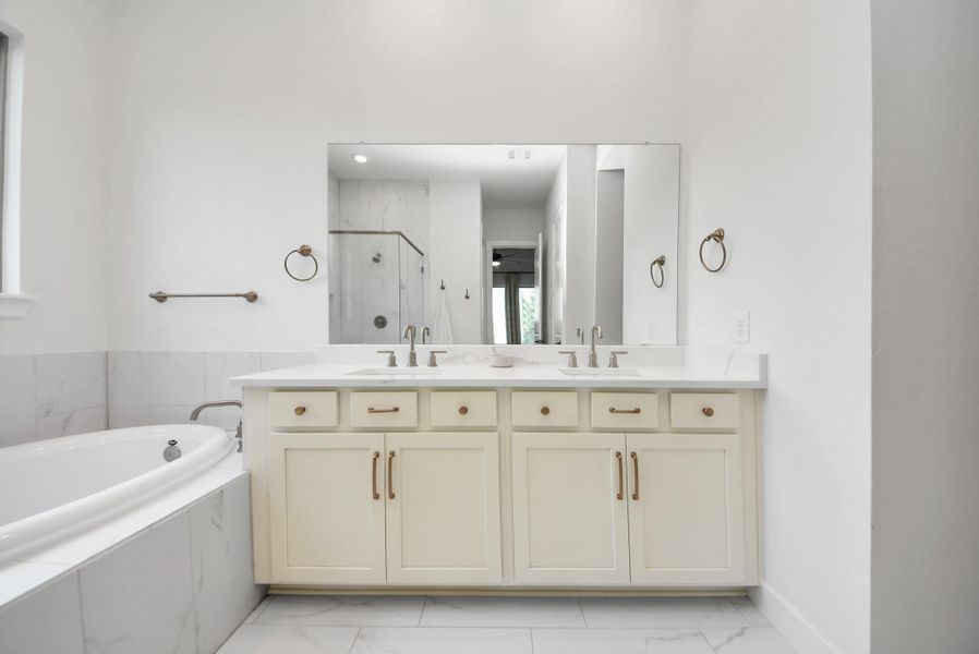 Bright and spacious bathroom featuring a double vanity with elegant fixtures, a large mirror, a luxurious soaking tub, and a modern glass-enclosed shower.