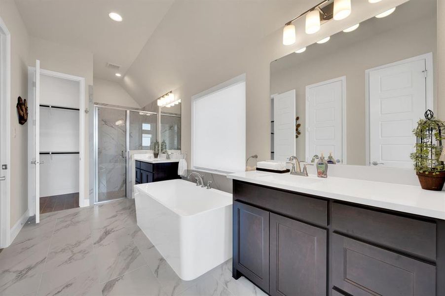 Primary En Suite Bath boasts a private water closet, linen cabinet, 2 walk in closets, separate vanities , an upgraded soaking free stand tub, walk in shower with bench and wood look tile floors.