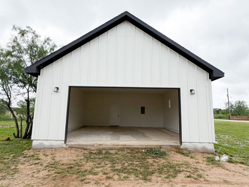 Detached garage featuring white board-and-batten siding, a black gable roof, and two exterior wall sconces Detached garage featuring white board-and-batten siding, a black gable roof, and two exterior wall sconces